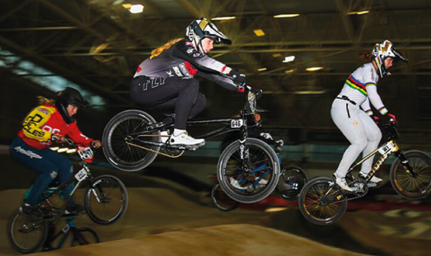 Women racing BMX bikes around an indoor track
